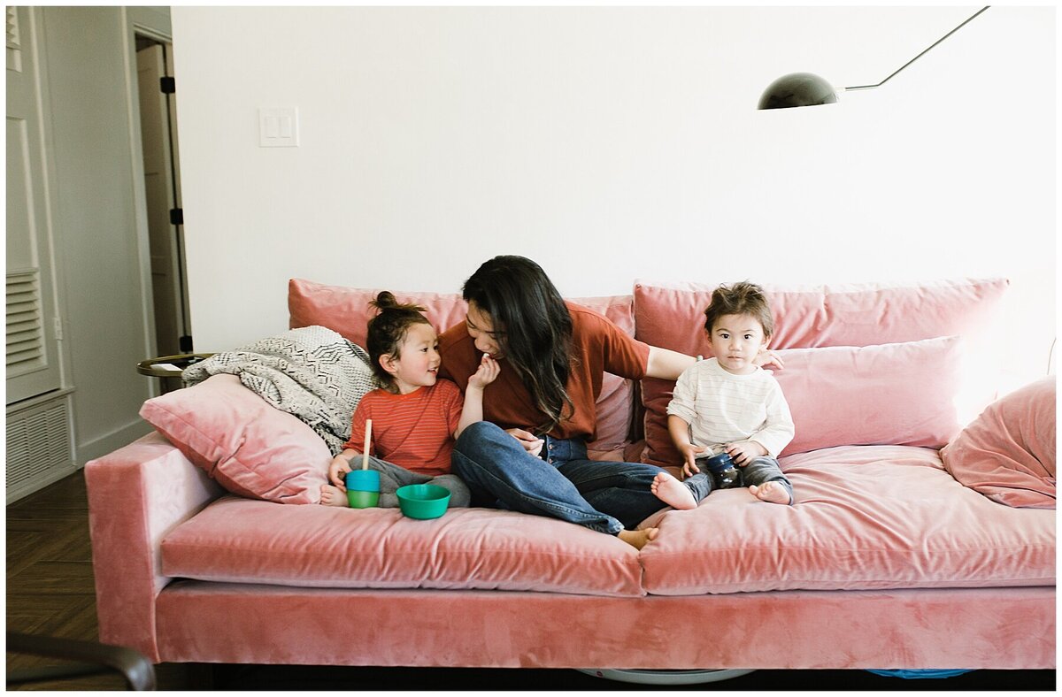 Mother sitting in-between two children on pink velvet sofa