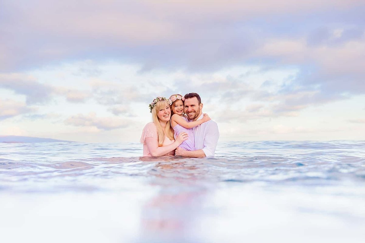 Family photograph of a Maui mom and dad with their young daughter waist deep in the ocean