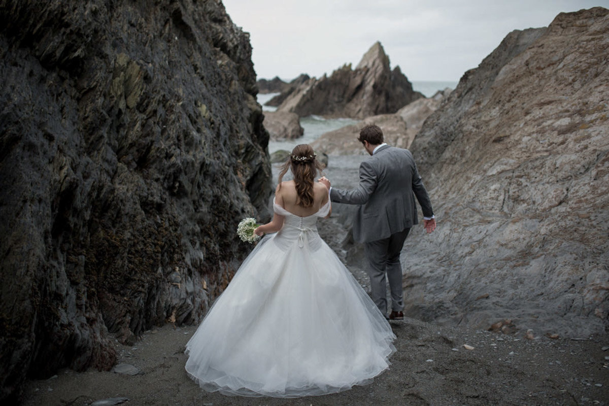 Groom helping his Bride through the rocks at Tunnels Beaches