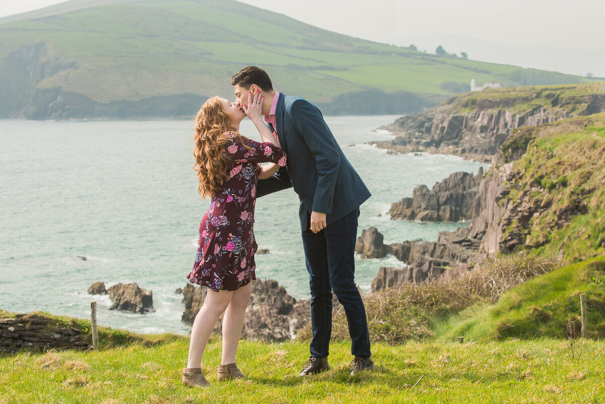 Young couple with red hair kissing in a field overlooking the sea
