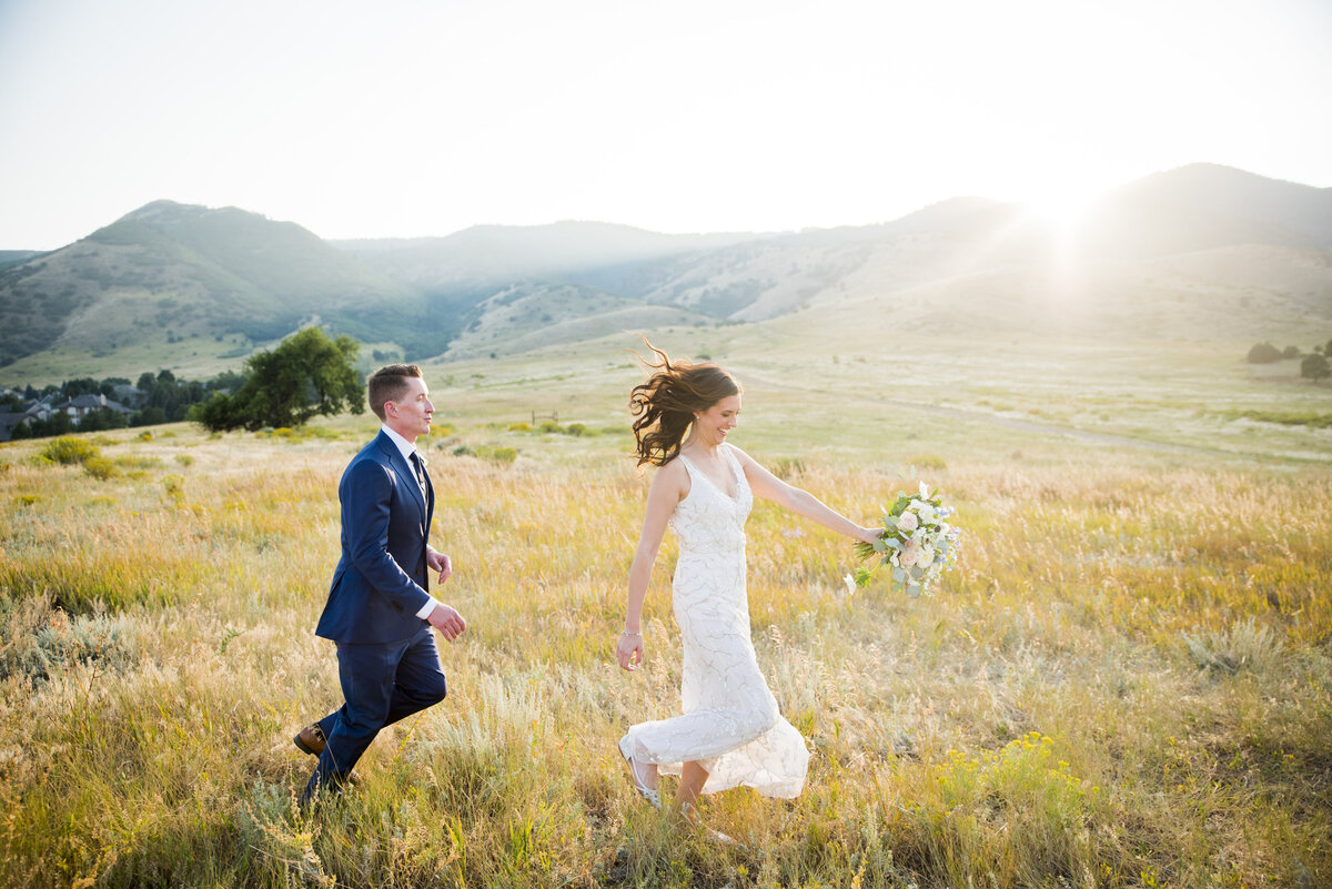 A groom playfully chases his bride through a field at golden hour at The Manor House in Littleton, Colorado.