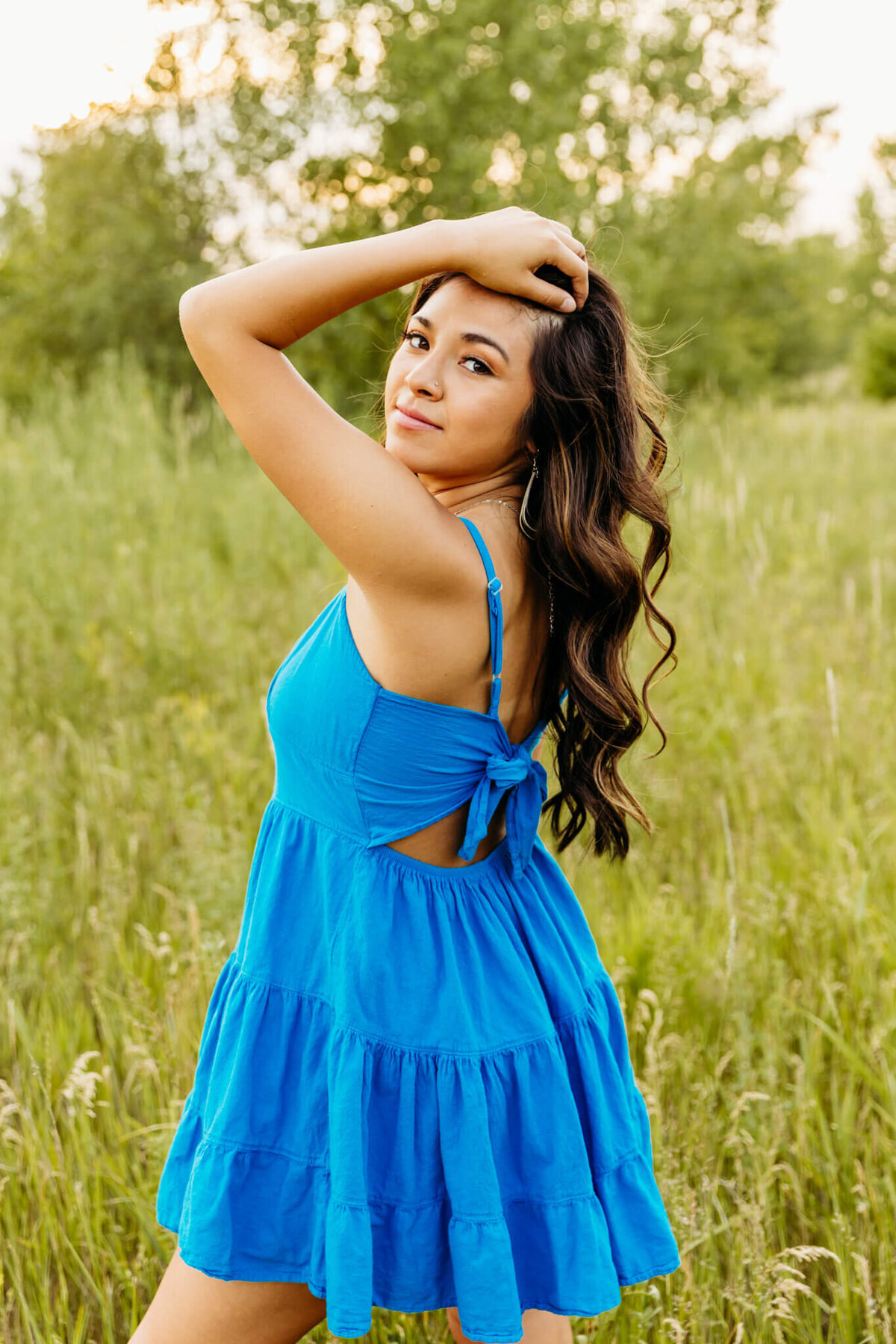 beautiful teen girl with brown hair posing with hand in her hair and looking through arm for senior photos