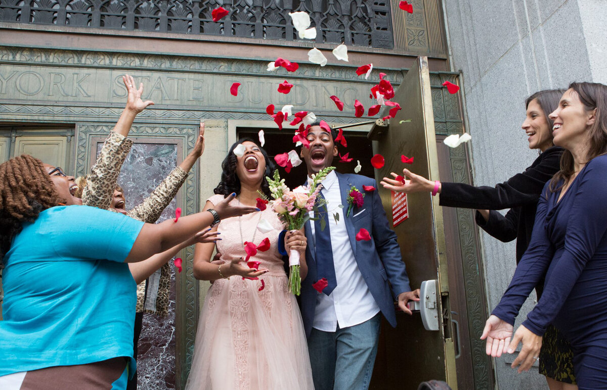 Newlyweds in a pink dress and blue suit run through red rose petals after their courthouse wedding in New York City wedding photographer Milestone Images