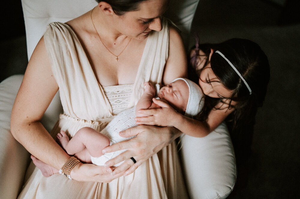 Mother and big sister lovingly holding newborn during a natural, in-home newborn session, capturing an intimate family bond in Portland.