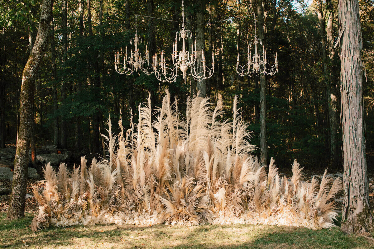Wheat and ivory pampas grass wedding ceremony aisle outside with chandeliers.