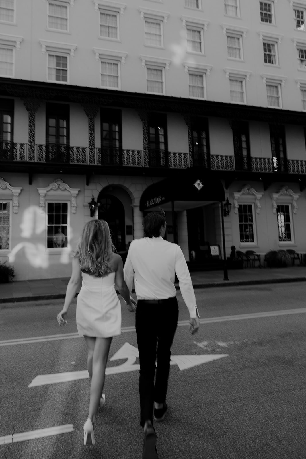 Couple crossing street and walking towards Mills House Charleston during engagement photo session in Charleston