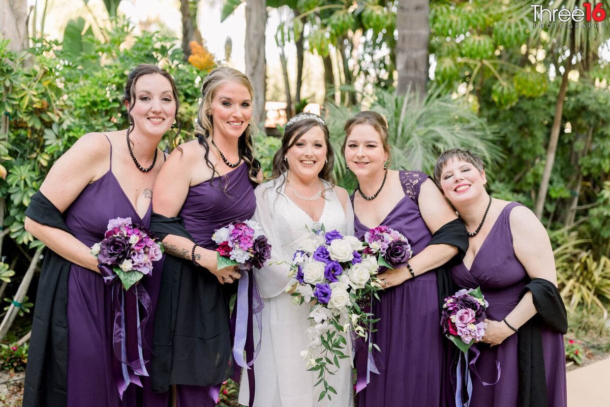 Bride poses with her dressed in purple Bridesmaids