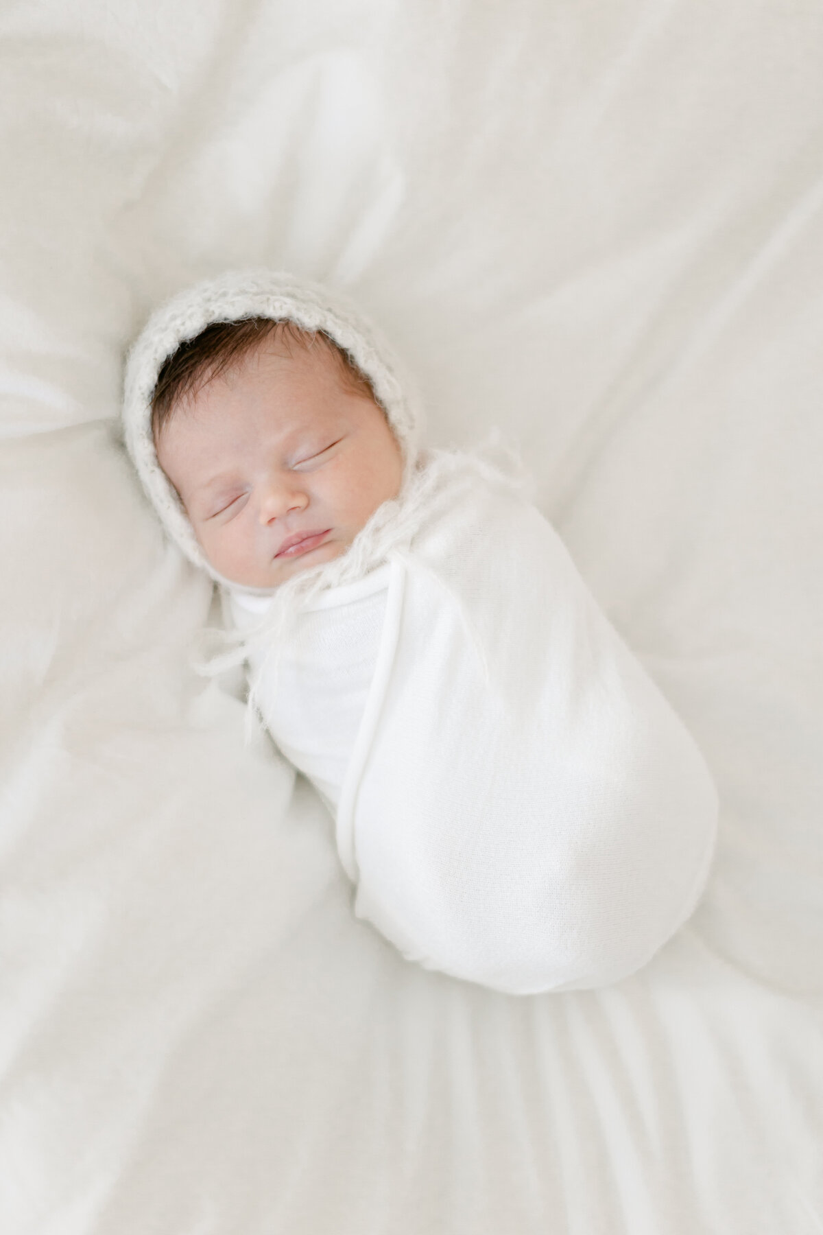 Newborn baby wearing a bonnet laying on a bed photographed by South Jersey Newborn Photographer Tara Federico