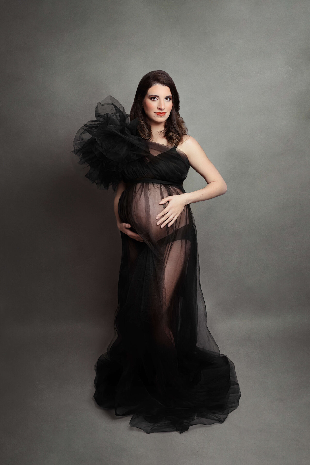 pregnant mother wearing a tulle black sheer maternity gown at her maternity photography session at a maternity photo studio