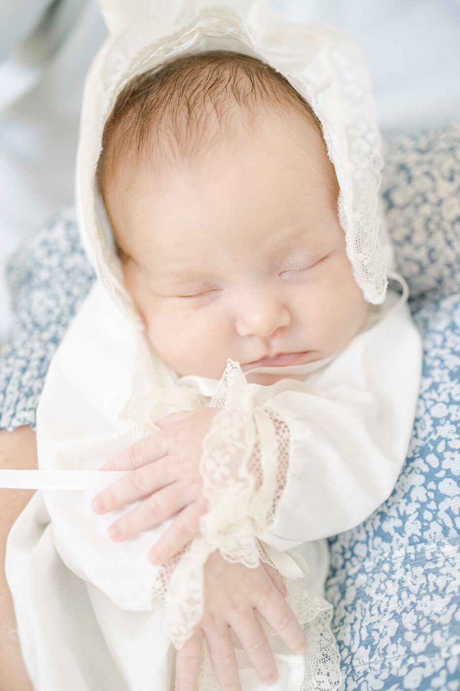 Newborn baby in heirloom daygown and bonnet sleeping in her mother's arms
