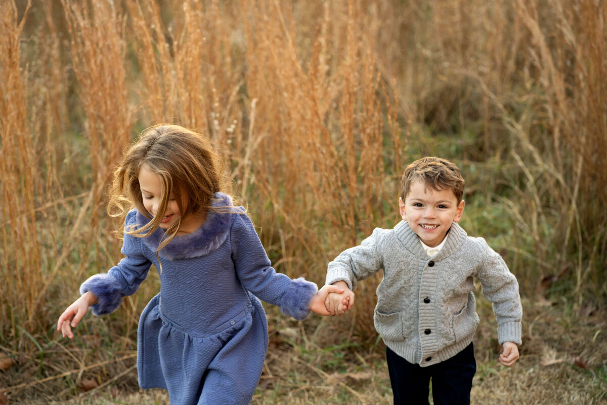 Young girl and boy holding hands while running through field of tall grass