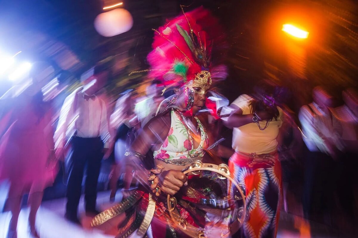 A dynamic shot of a dancer in vibrant, feathered carnival attire performing at a wedding, with guests and motion blur adding to the energy of the scene.