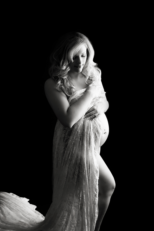 A mother to be wrapped in a sheet stands in a studio with the bump exposed thanks to a New Jersey Maternity Photographer