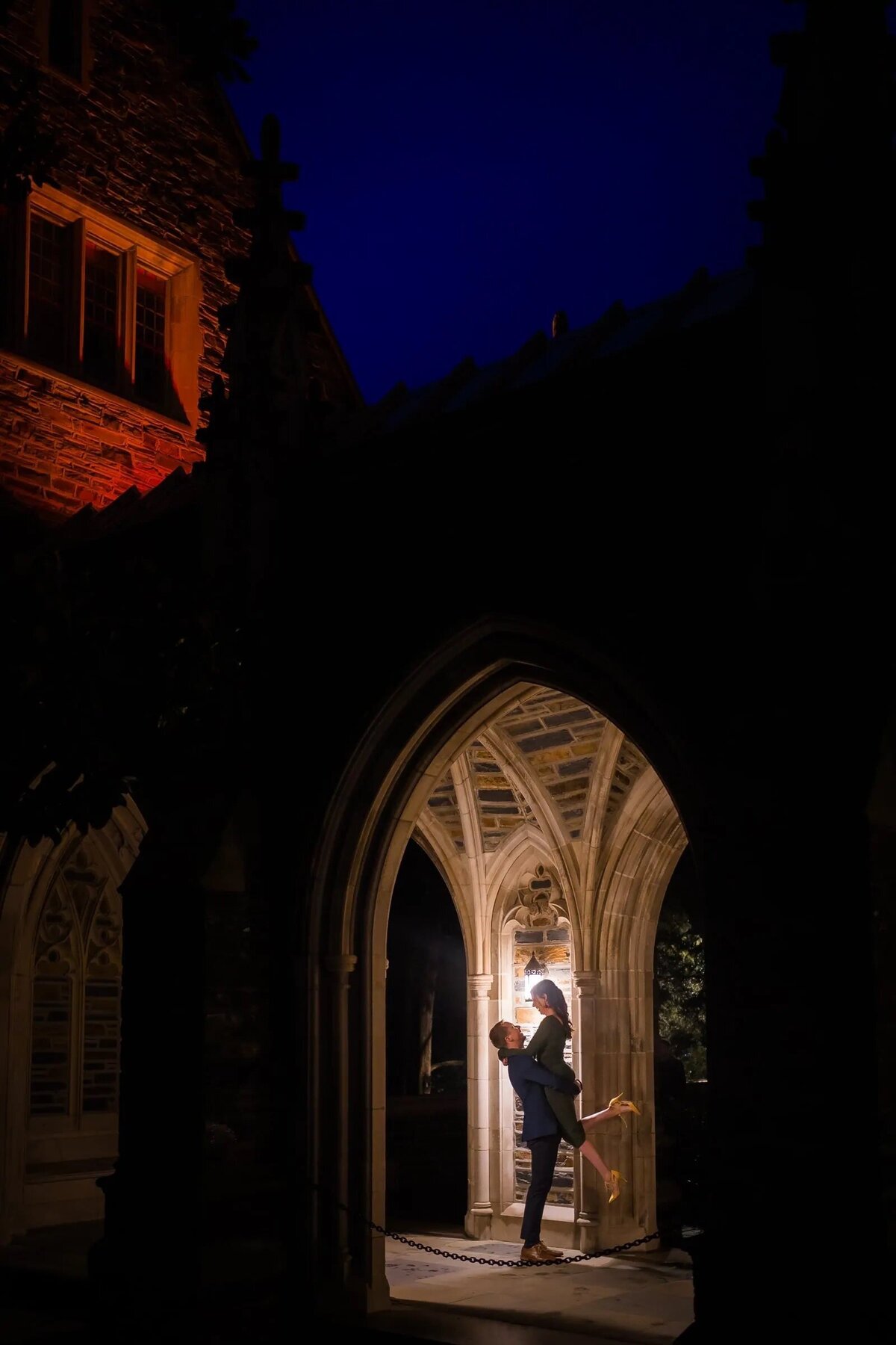 Couple in an arched doorway, with a man lifting a woman off the ground, backlit by the night sky