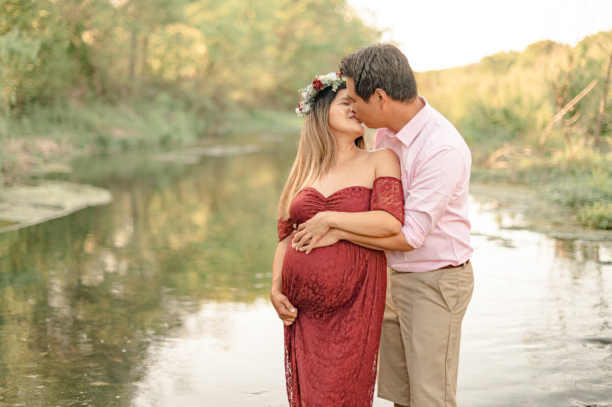Expectant couple kisses in a creek at golden hour during photos with San Antonio maternity photographer Cassey Golden.