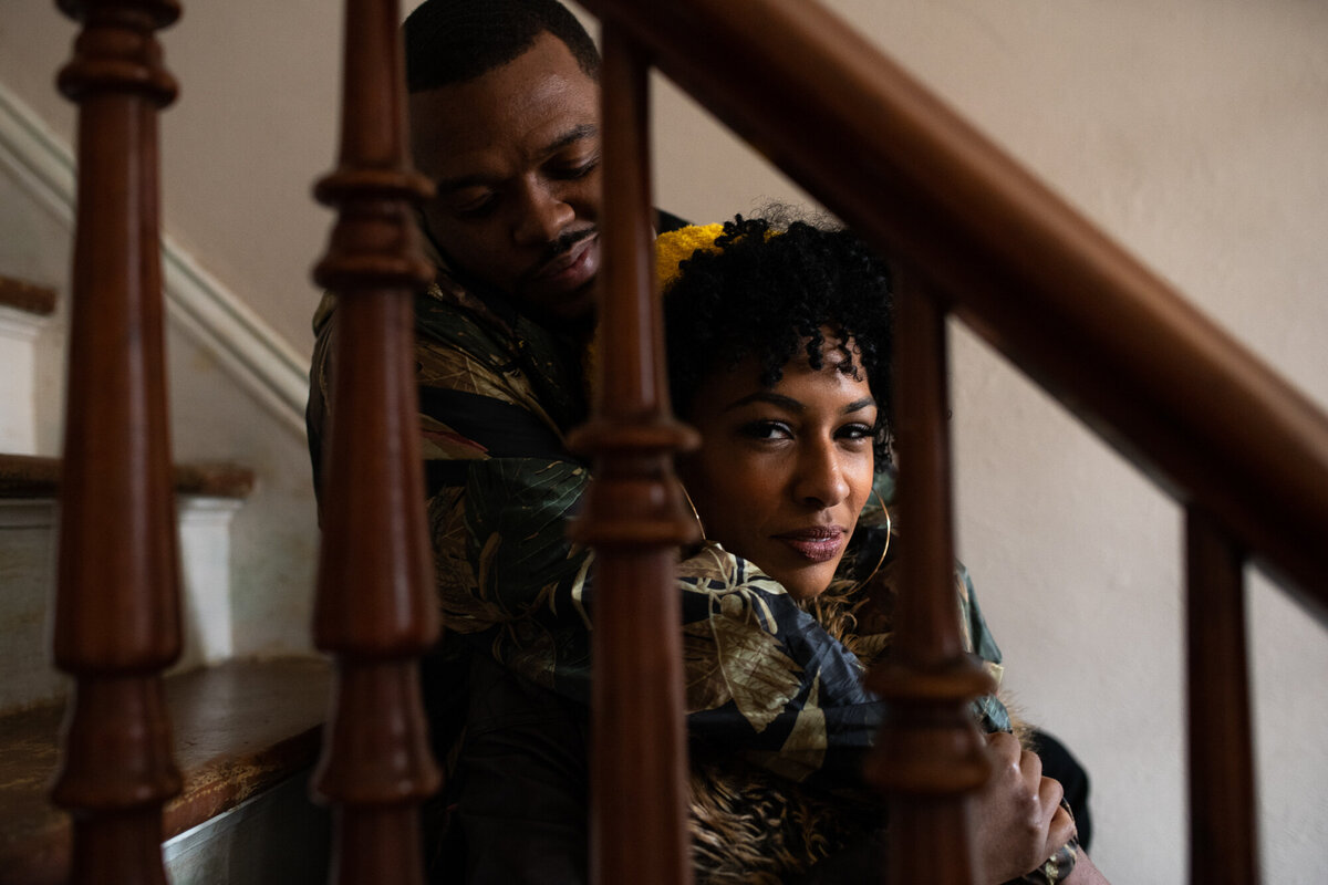 Couple snuggles on the stairs at their in home engagement session