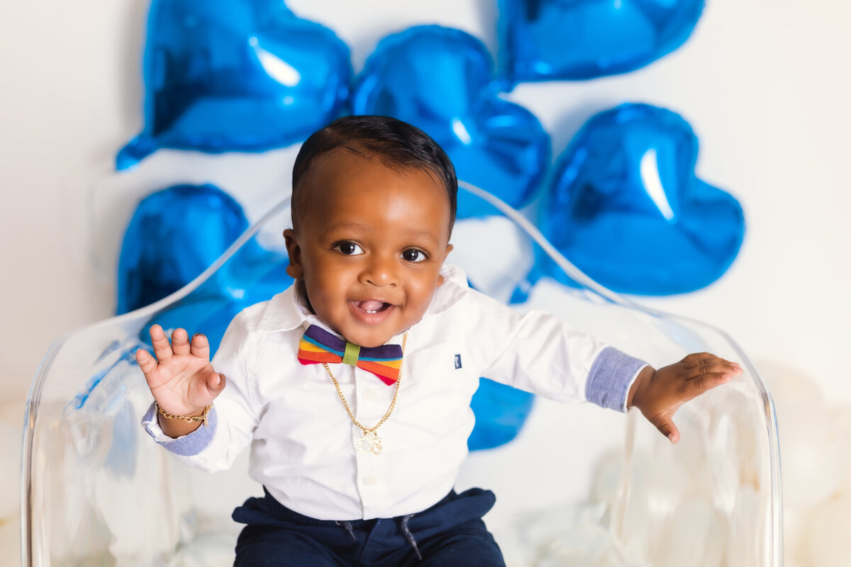 Cake Smash Photographer, a baby boy smiles and wears a rainbow bow tie