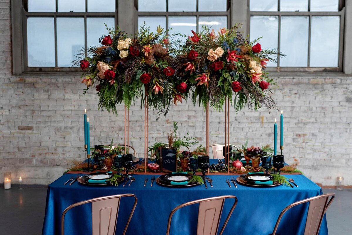 a very pretty flower arrangement is elevated above a reception table by flowers by alana