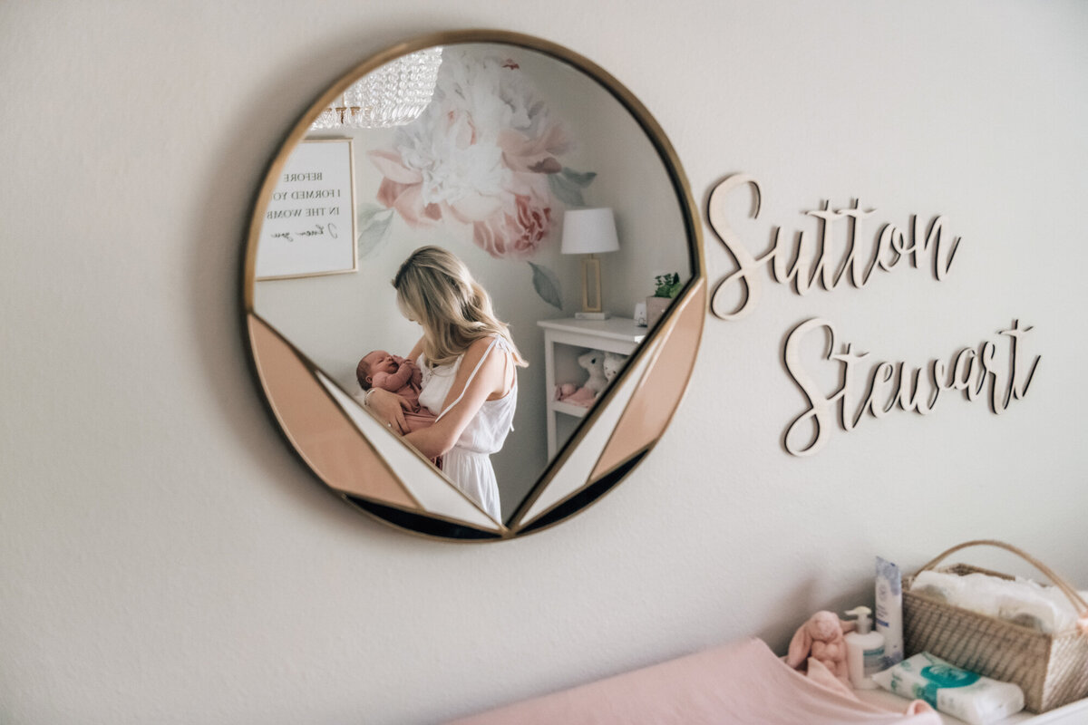 Newborn Photography, Mom holding baby girl in the mirror with the baby girl's name, Sutton Stewart, on the wall next to the mirror.