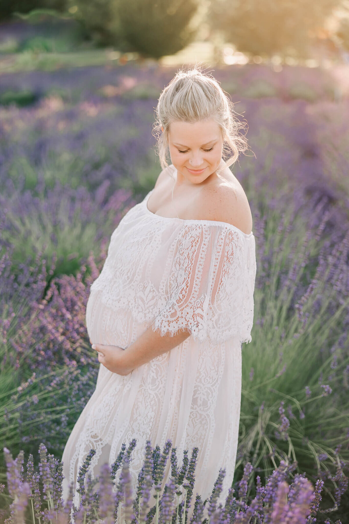 pregnant woman wearing white dress in lavender field at sunset.