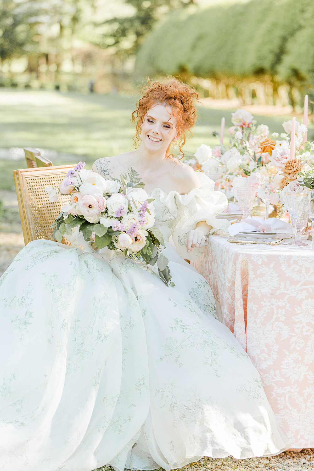 A bride sits at a table at an estate in Boston's North Shore. the bride is laughing and holding her bouquet. Captured by best Massachusetts wedding photographer Lia Rose Weddings