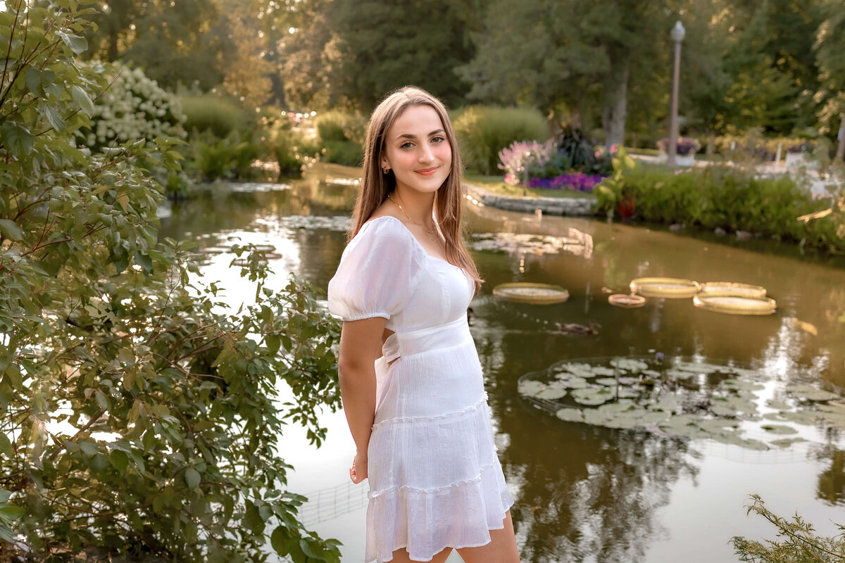 A brown haired girl is standing next to the lily pond  in tower grove park.