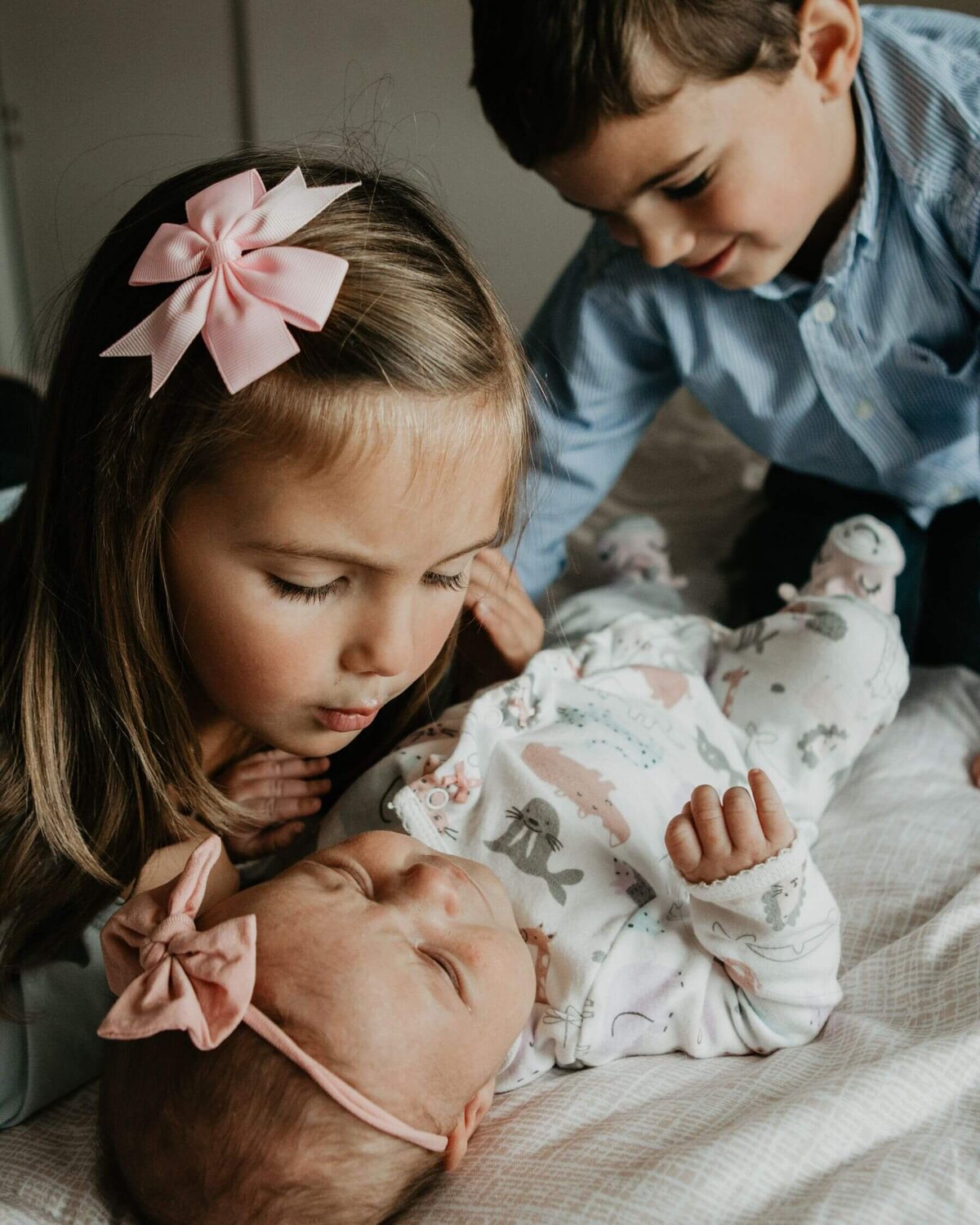 A big brother and sister looking down at their new baby sister and smiling. Lifestyle photography by Tracy Miller Photography