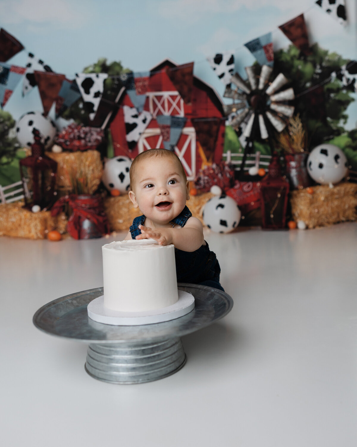 Farm-themed first birthday session with a baby boy digging into his cake, smiling with frosting all over.
Photograph by Yucaipa cake smash photographer Kaitlyn Dawn Photography.