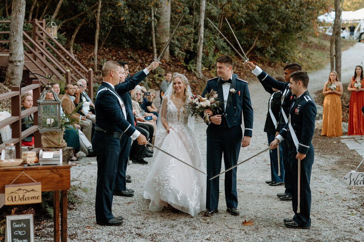 groomsmen in uniform holding up swords as bride and groom walk through