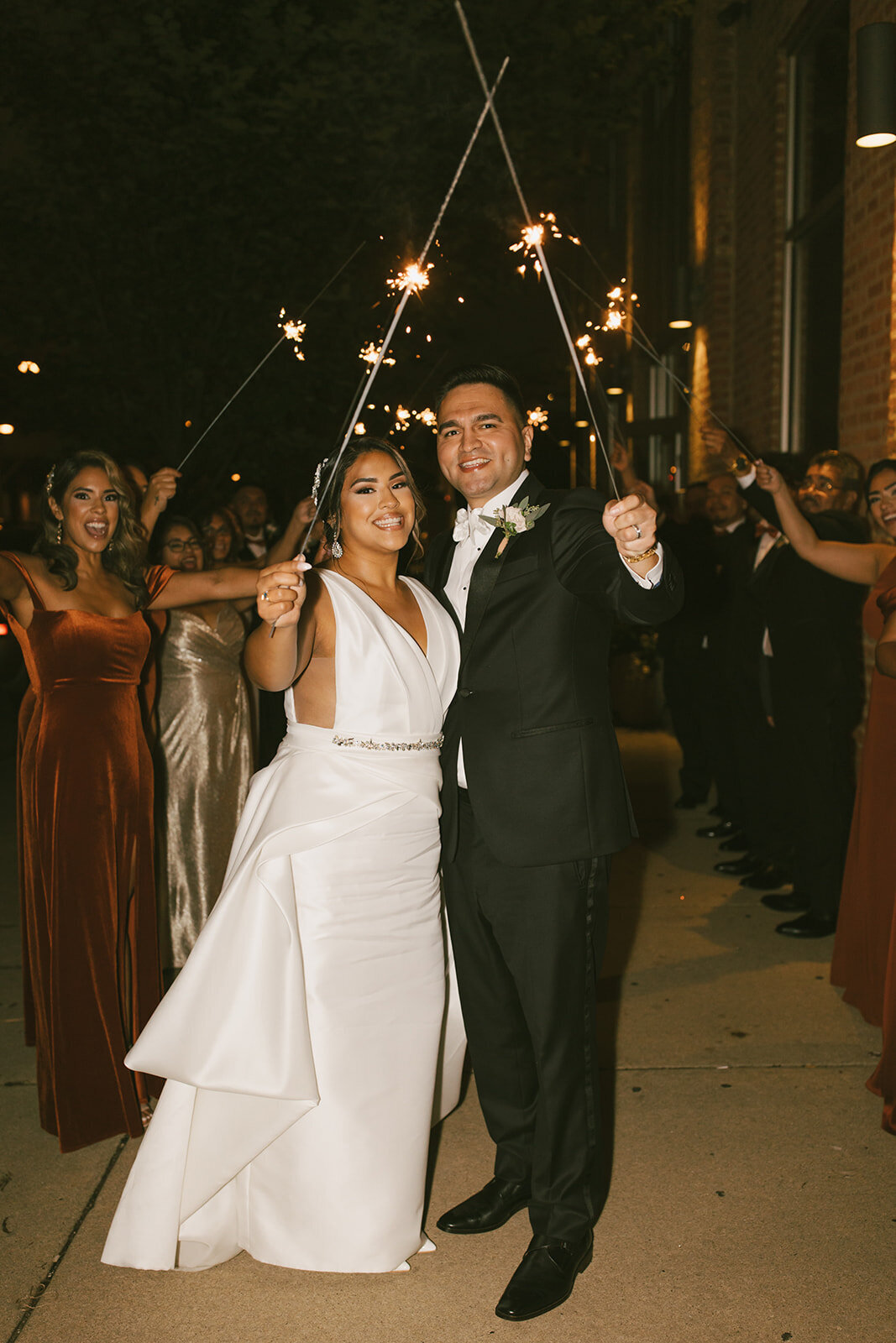 Newlywed bride and groom smile at the  camera and hold sparklers after Loft on Lake wedding reception.
