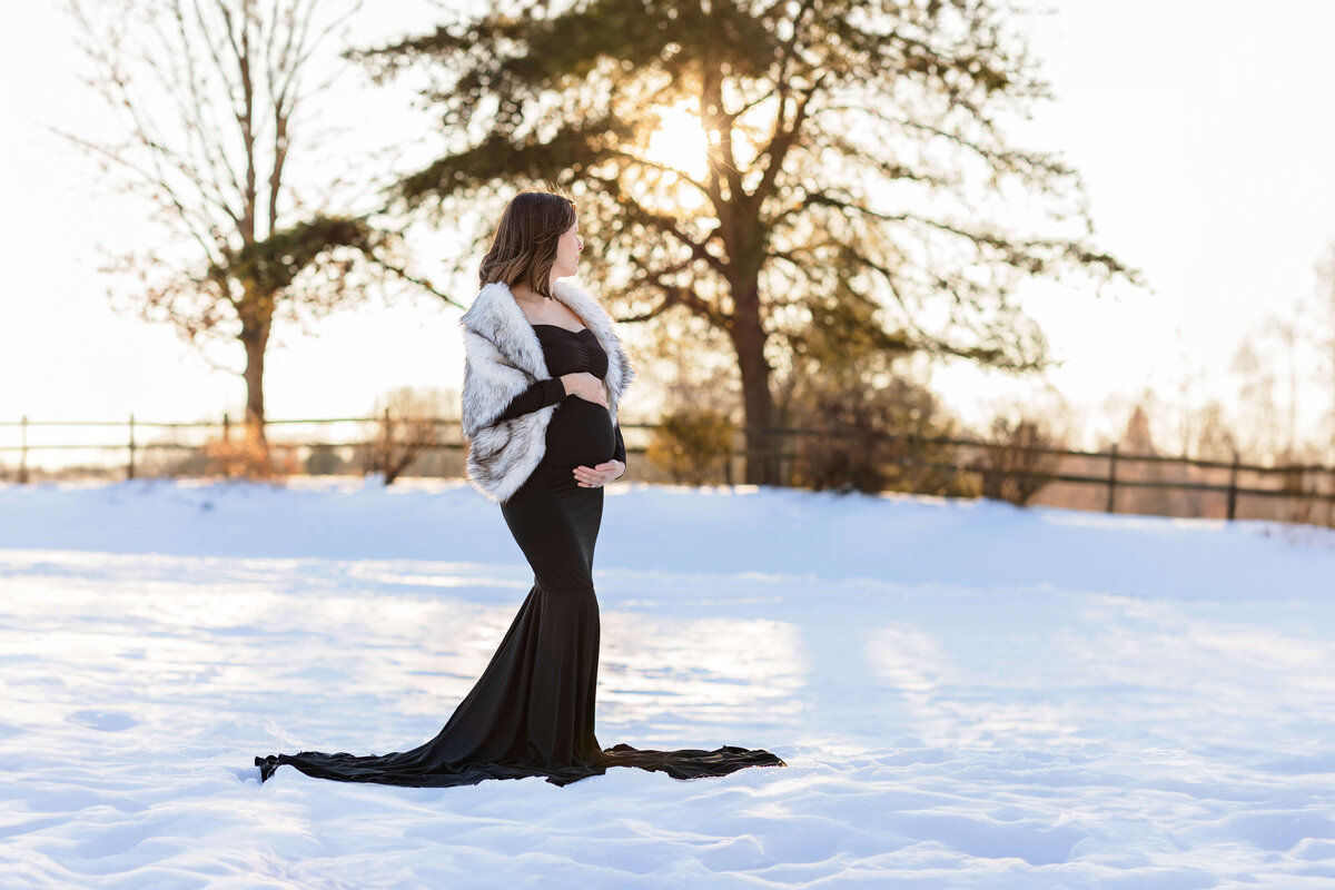 A pregnant woman hugging her belly in a snowy field at a Burke, VA maternity photo session.