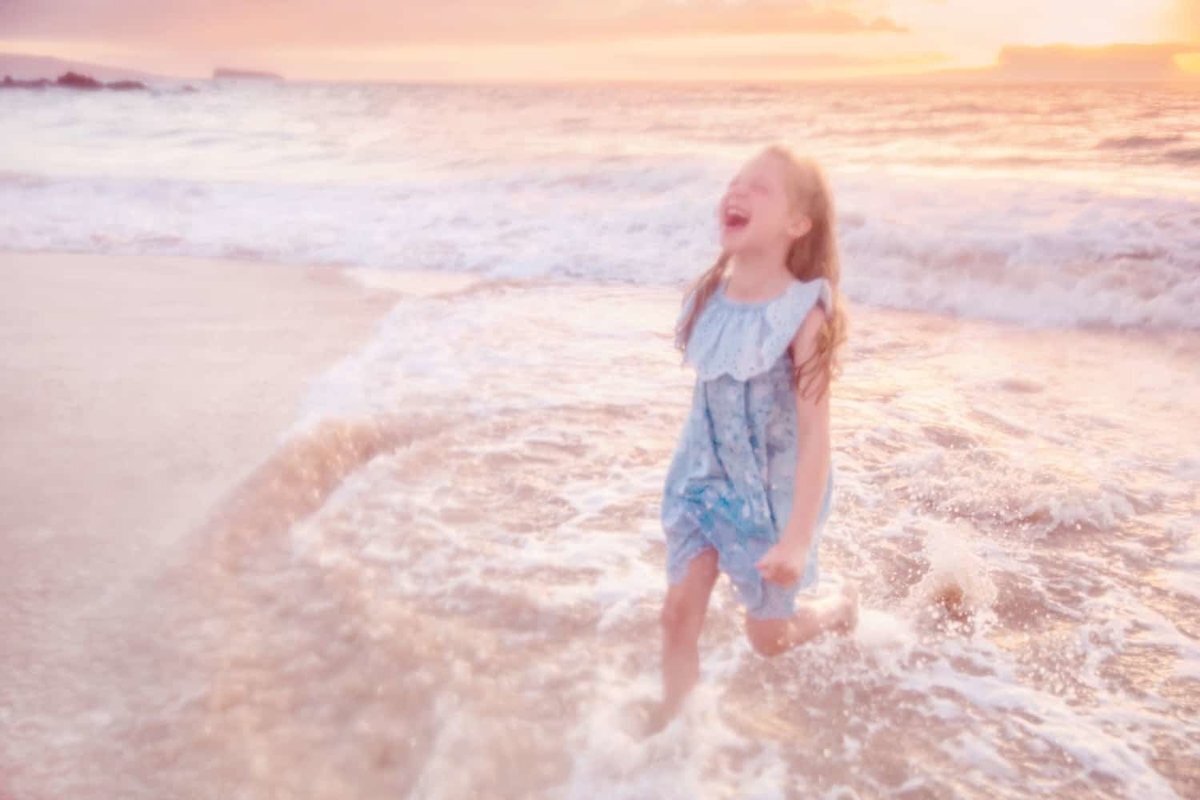 Intentionally blurry image of girl laughing and running on the beach on Maui with her family off camera