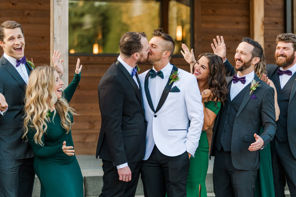 Two-grooms-kiss-as-wedding-party-cheer-outside-Liljebeck-Farms-Wedding-venue-in-Woodinville-photo-by-Joanna-Monger-Photography