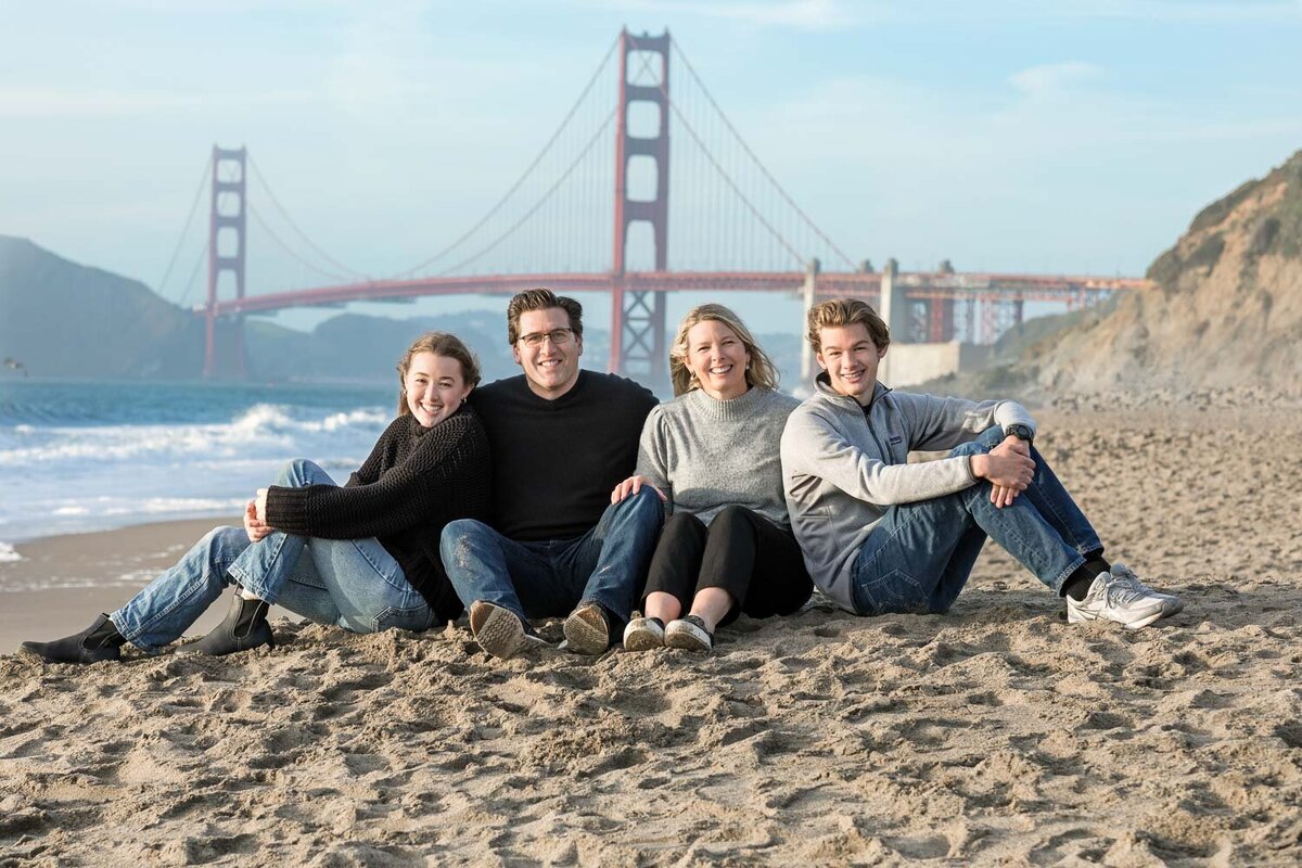 family sitting on the beach by golden gate