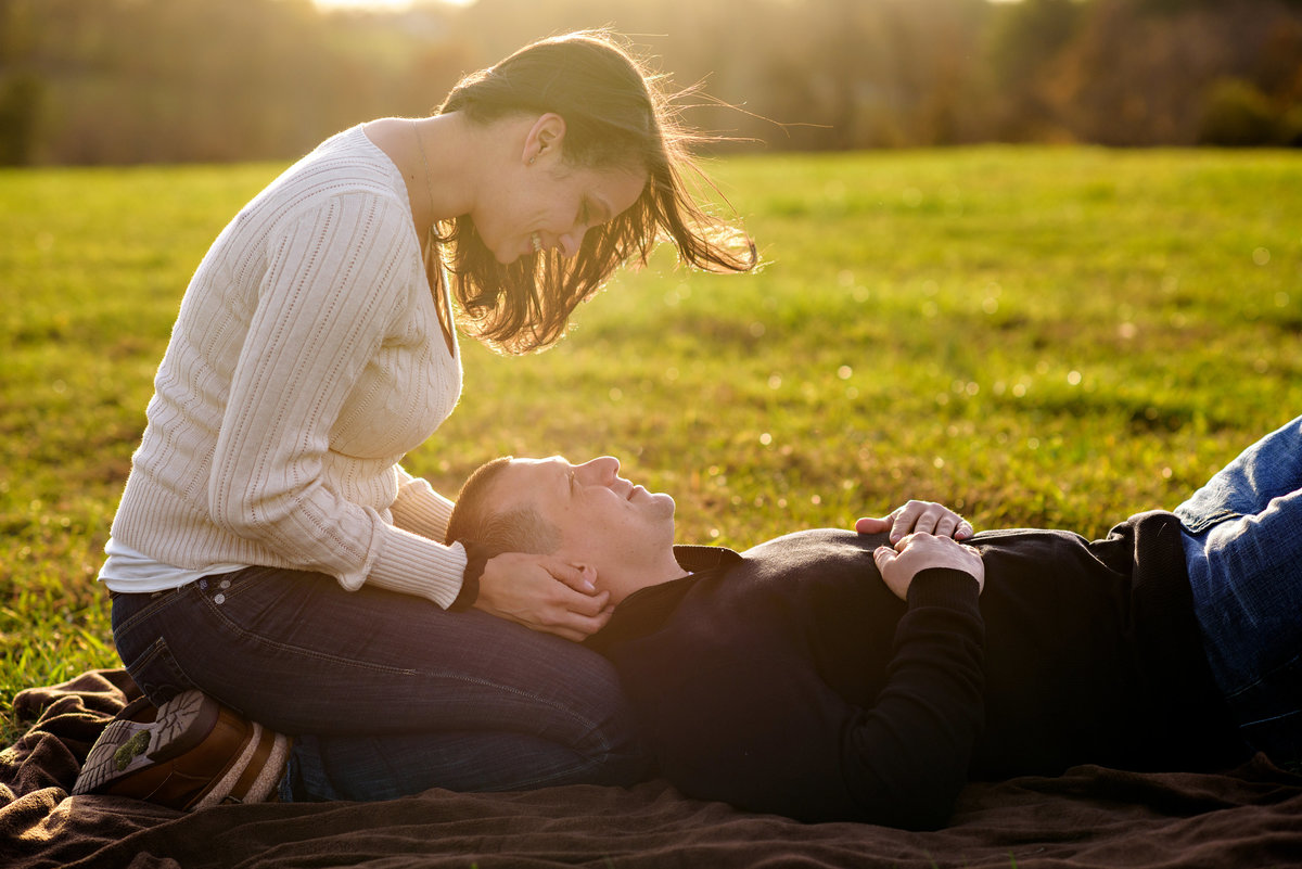 A man lays in his fiance's lap while she looks into his eyes.