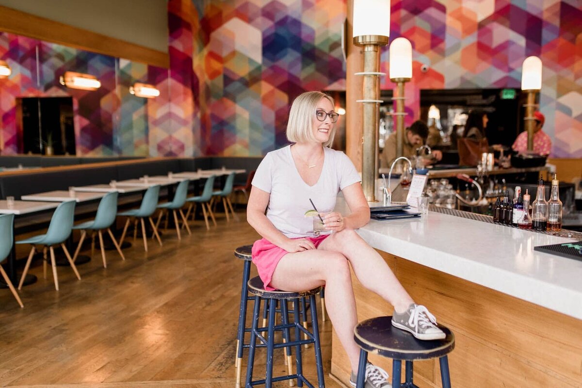 crystal genes photography sits at a bar drinking a tequila soda with a colorful mural behind her at capitol
