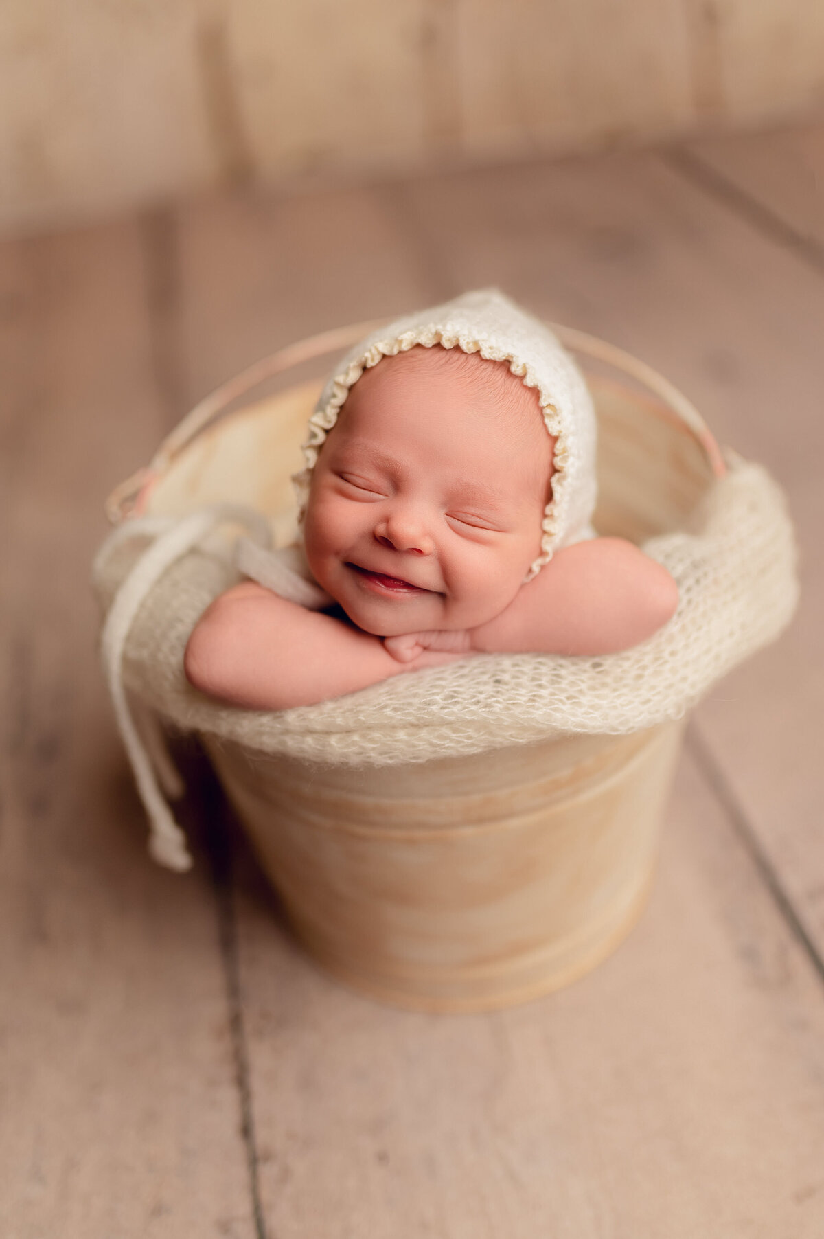 Portrait of infant sleeping in a bucket wearing a knit bonnet and a huge smile.