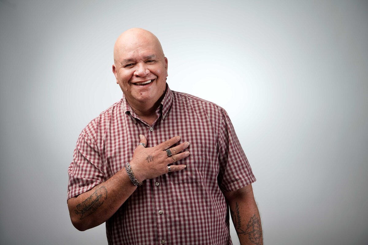A smiling man with hand over heart who was homeless is photographed in studio on a white backdrop for Father Joes Villages.