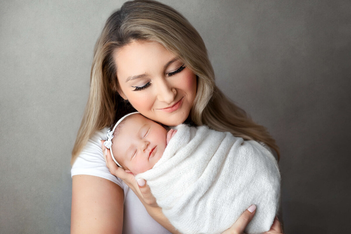 new mom holding her newborn baby girl  wearing  white on a grey backdrop at their VA Newborn  Photoshoot