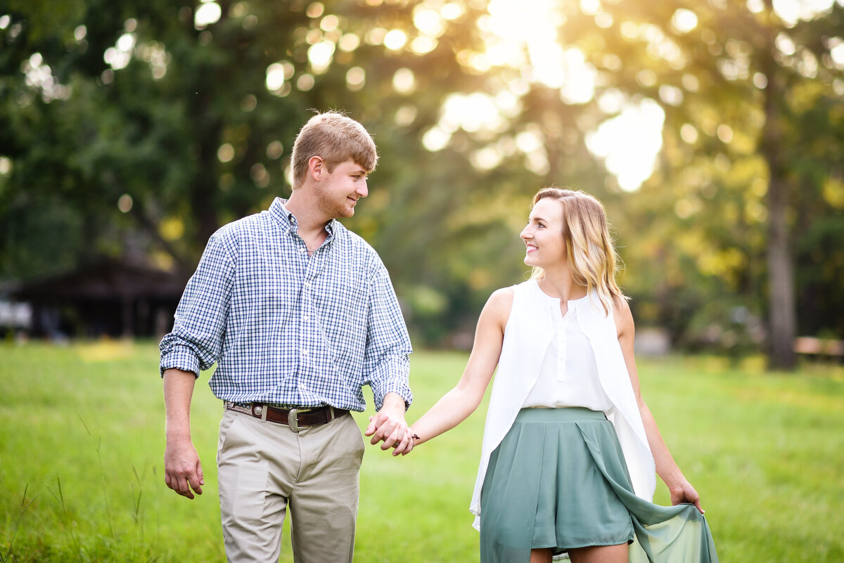 Beautiful Mississippi Engagement Photography: Couple walks hand-in-hand in a field during sunset