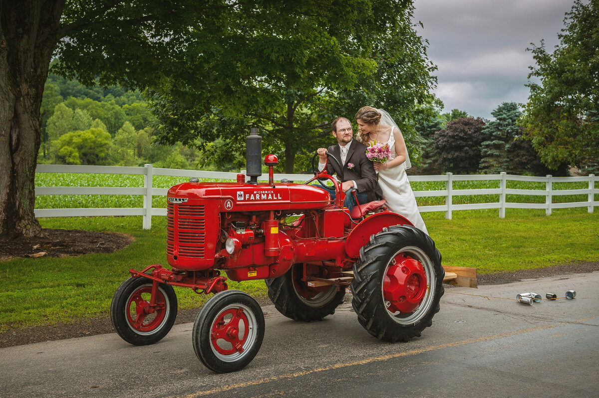 Bride and groom riding a tractor dragging tin cans behind.