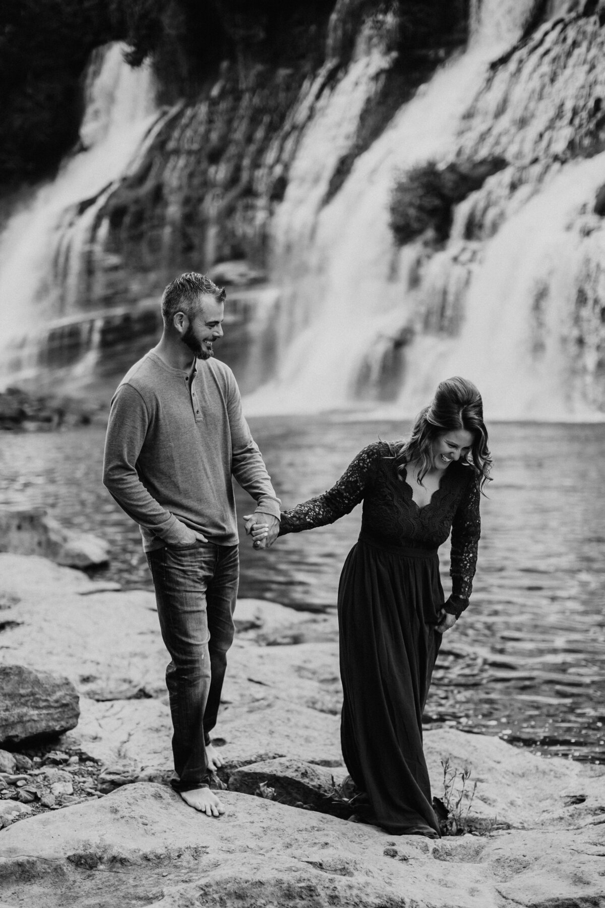 couple laughing and holding hands by a waterfall