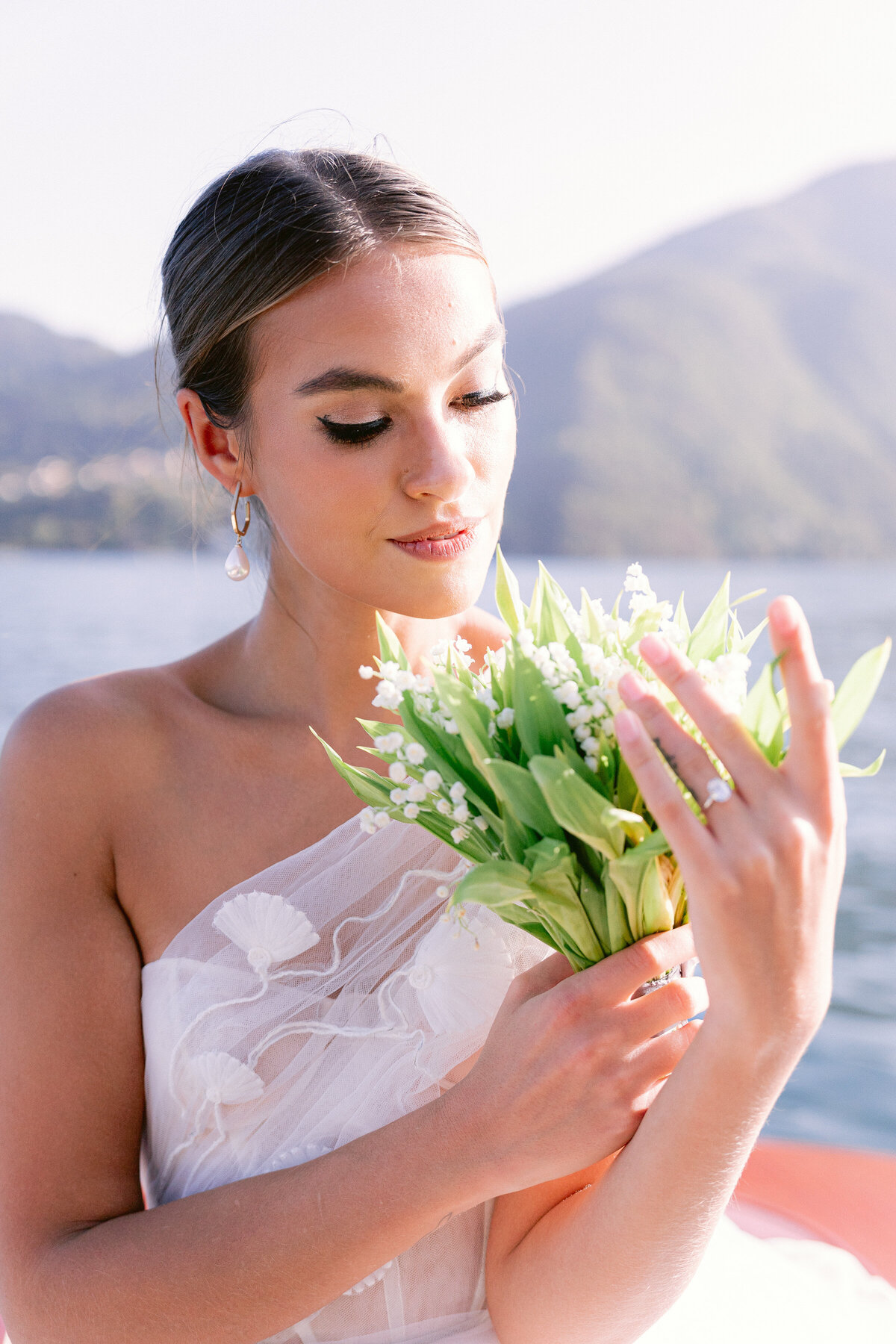 Bride holding small bouquet of white florals with greenery on a private boat on lake como, italy