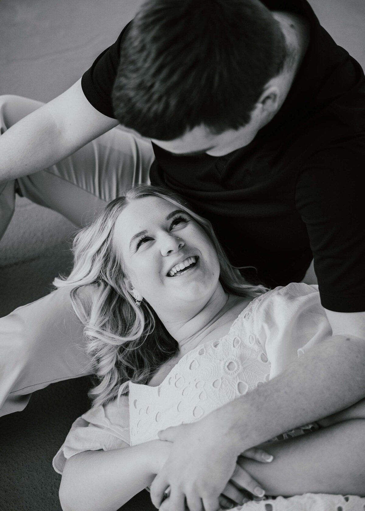 Maddie Rae Photography black and white up close of a couple. he is sitting and she is laying on one of his legs looking up at him smiling. taken from above them