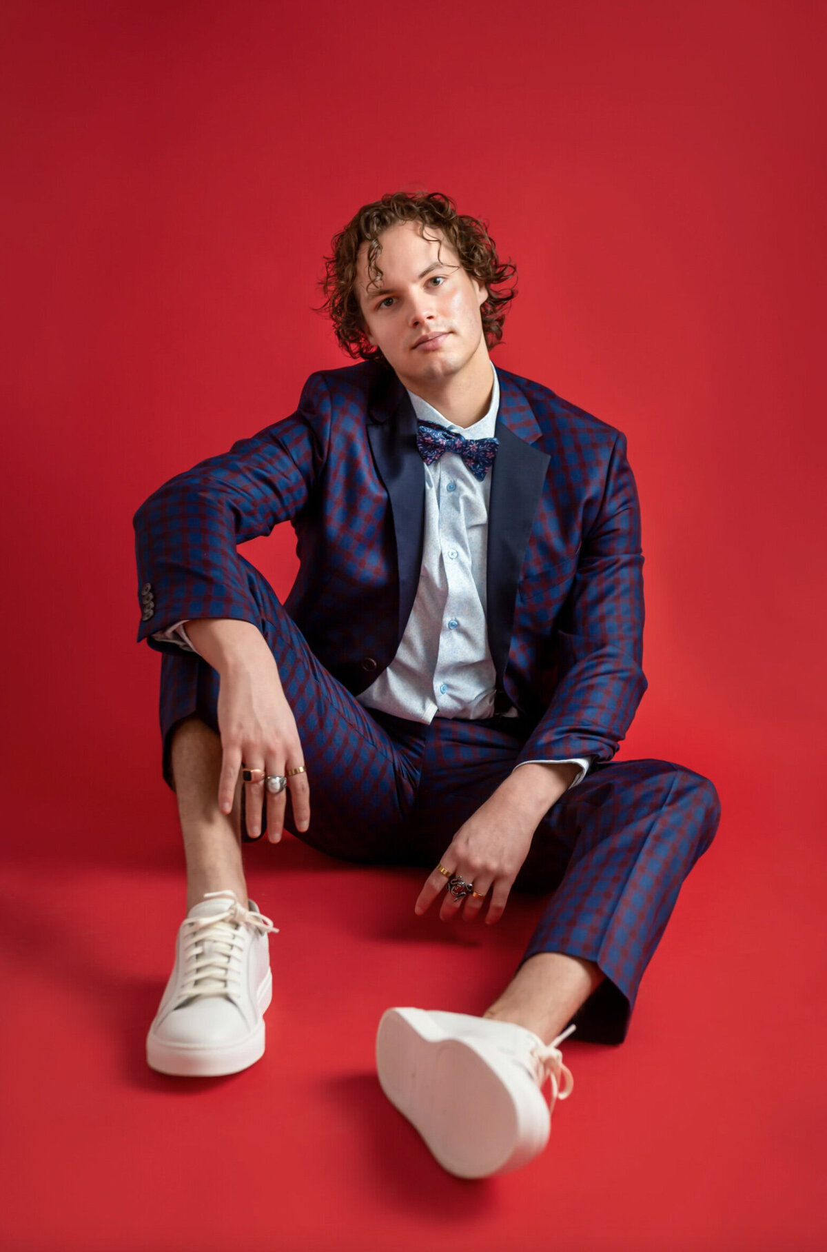 Man in a blue and purple plaid suit, sitting on a red backdrop at a New Jersey headshot studio