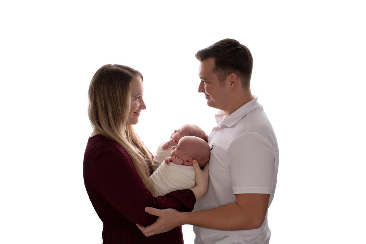 Gulf Breeze FL Newborn Photographer backlit image of parents embracing twins during studio session.