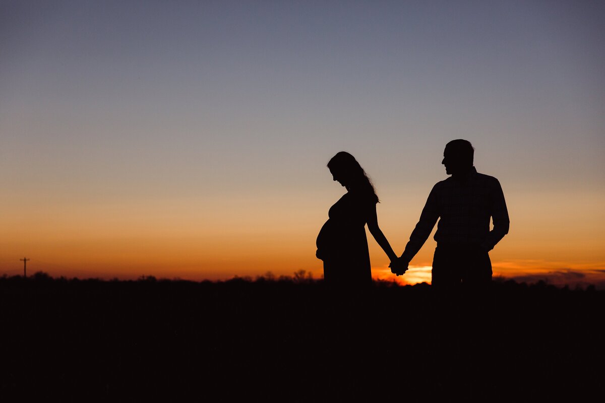 Sunset silhouette of pregnant woman and husband holding hands during a maternity photo session in Lexington.