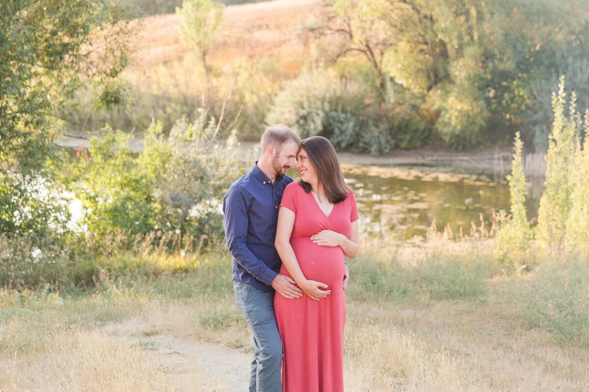 husband and wife snuggle while holding baby bump in Broomfield, CO