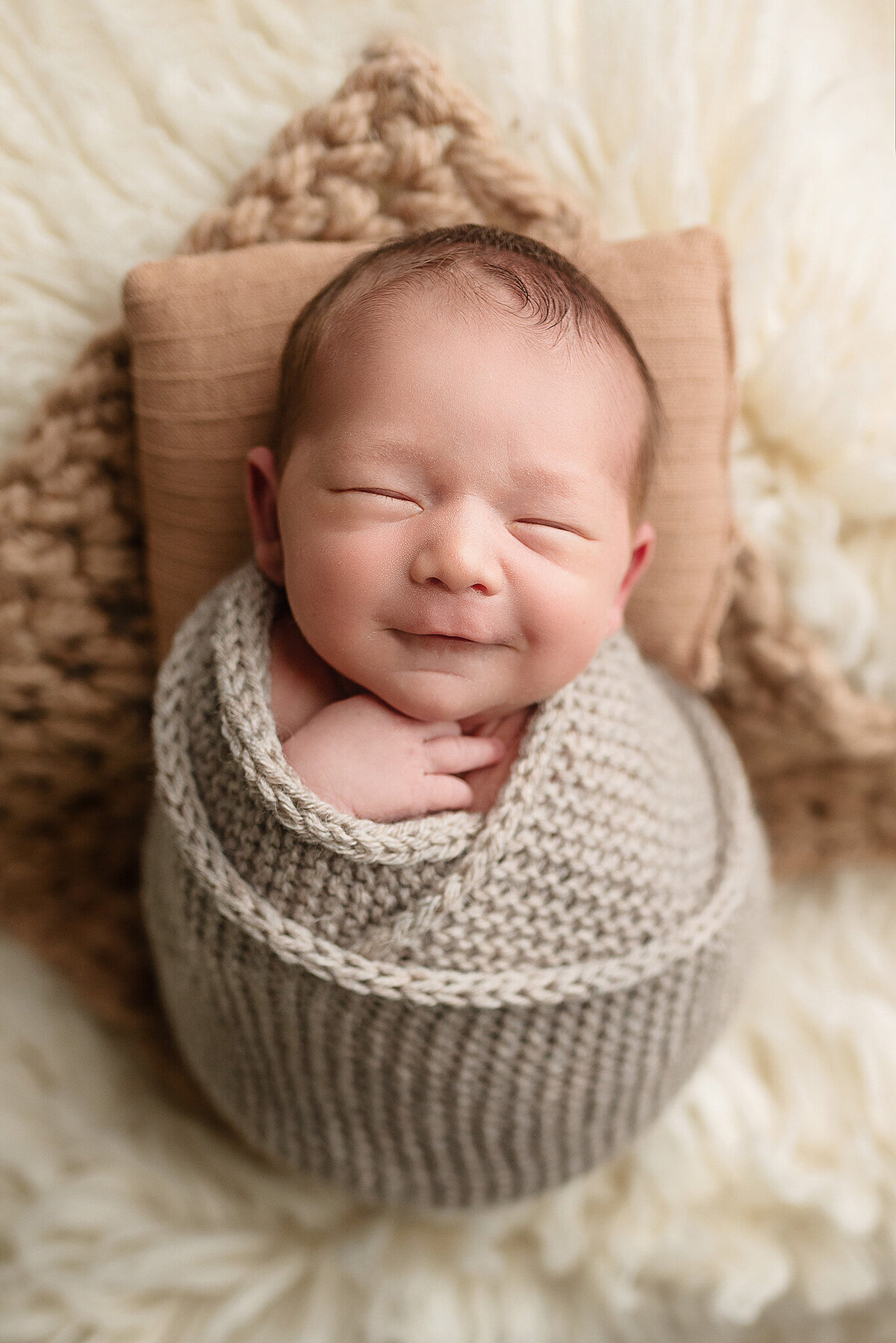 Wrapped newborn smiling during his newborn session at Jennifer Brandes Photography.