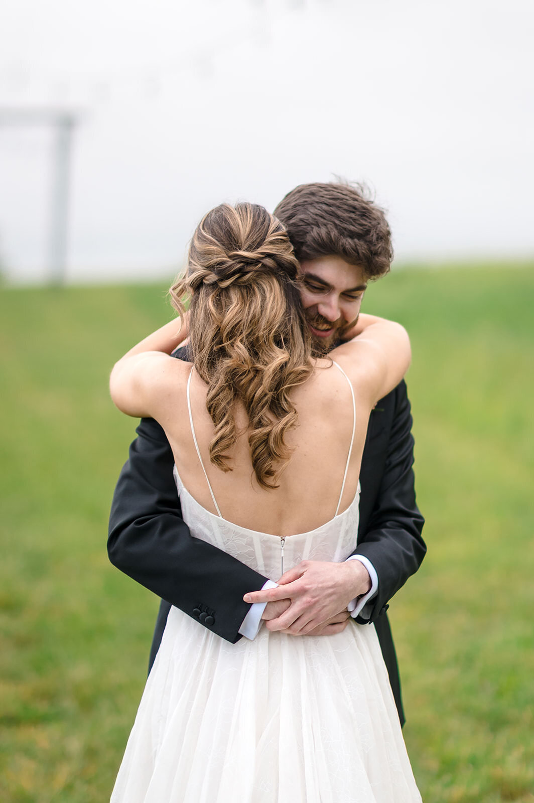 A bride and groom in a close embrace, with the bride's back turned to the camera, showcasing her updo hairstyle and the back of her dress.